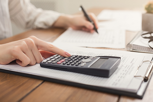 Woman sitting at a desk using calculator calculating if her client is achieving successful investing